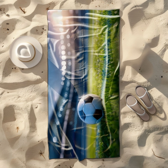 Ręcznik plażowy z motywem piłkarskim rozłożony na piasku obok letnich sandałów