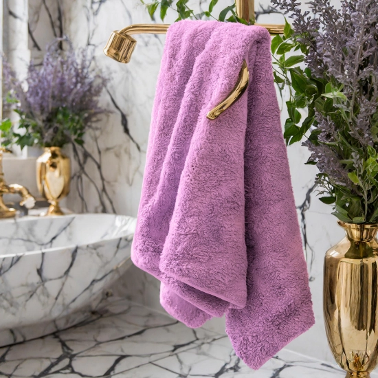 Elegancki, fioletowy ręcznik łazienkowy Rimini z bawełny zawieszony na złotym relingu w eleganckiej łazience.