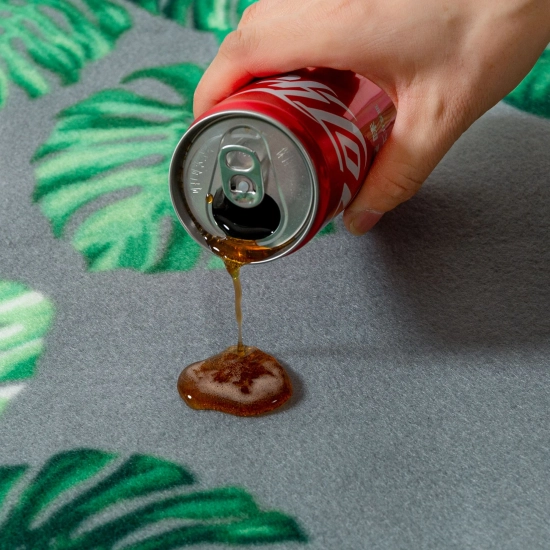 Ciemny napój wylewany z puszki, który perli się na polarowej powierzchni koca z motywem tropikalnym.