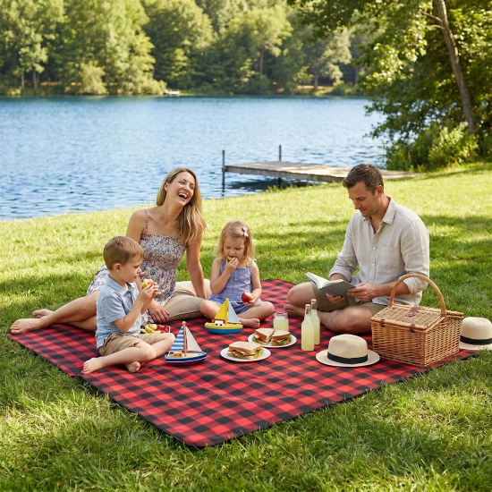 Rodzina z dziećmi jedząca piknik nad jeziorem na dużym kocu WONDER w czerwono-czarną kratkę.