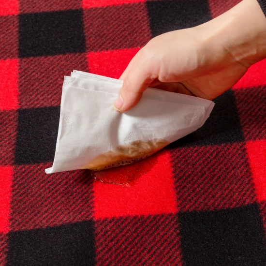 Łatwe i szybkie zbieranie rozlanego napoju z powierzchni koca piknikowego za pomocą ręcznika papierowego.