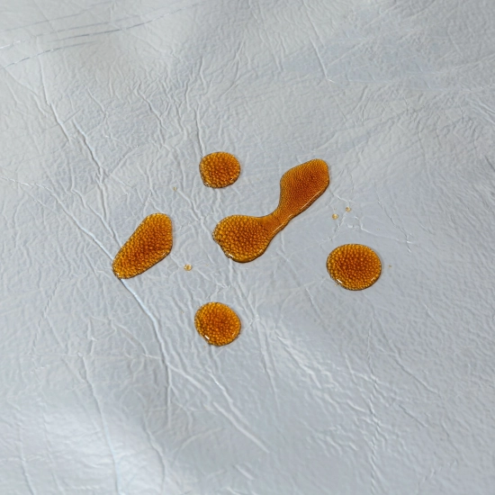 Zbliżenie na krople rozlanego płynu utrzymujące się na powłoce koca WONDER, zapobiegające szybkiemu wchłanianiu.