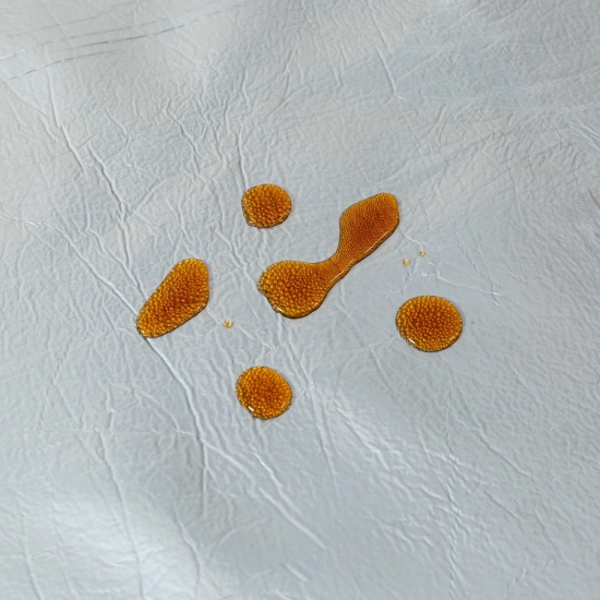 Zbliżenie na krople rozlanego płynu utrzymujące się na powłoce koca WONDER, zapobiegające szybkiemu wchłanianiu.