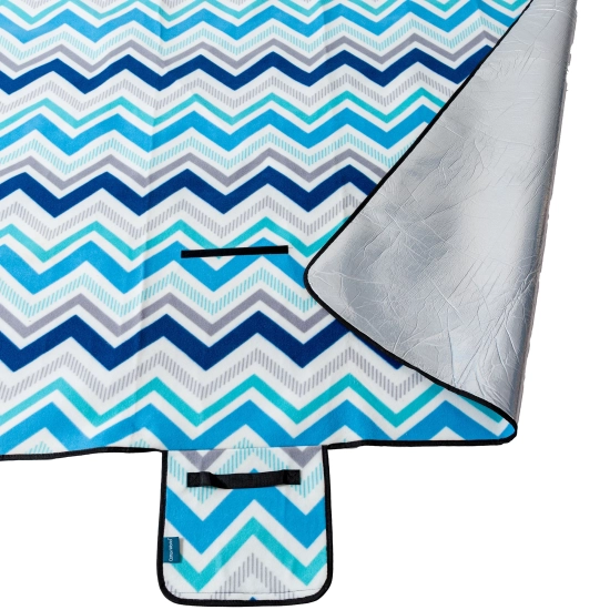 Odwinięty róg koca piknikowego prezentujący aluminiową warstwę od spodu chroniącą przed chłodem.