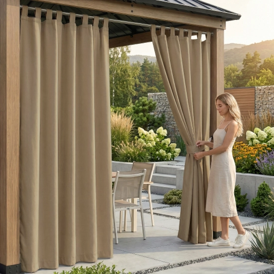 Kobieta na tarasie pod drewnianą pergolą upinająca wodoodporną, ciemnobeżową zasłonę ogrodową na szelkach