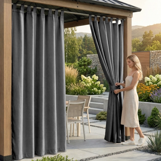 Kobieta pod drewnianą pergolą upinająca grafitową, wodoodporną zasłonę ogrodową na szelkach materiałowym paskiem